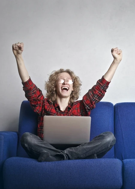 Person sat with a laptop lifting their arms up in joy