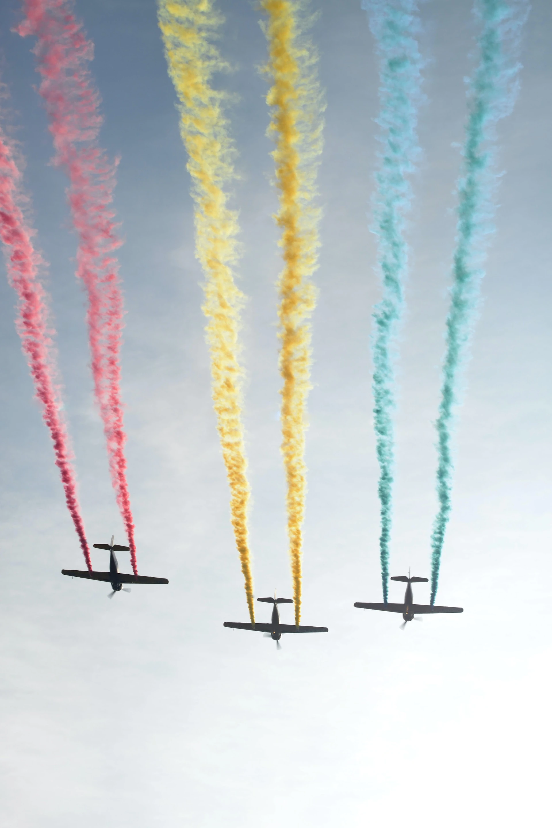 three planes flying through the sky with red, yellow, and blue smoke coming out of each plane respectively