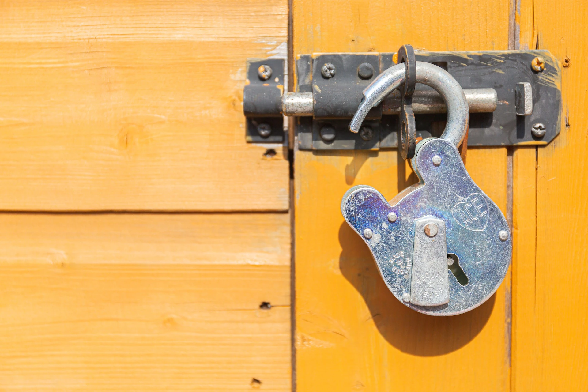 broken lock hanging off deadbolt against yellow wood background