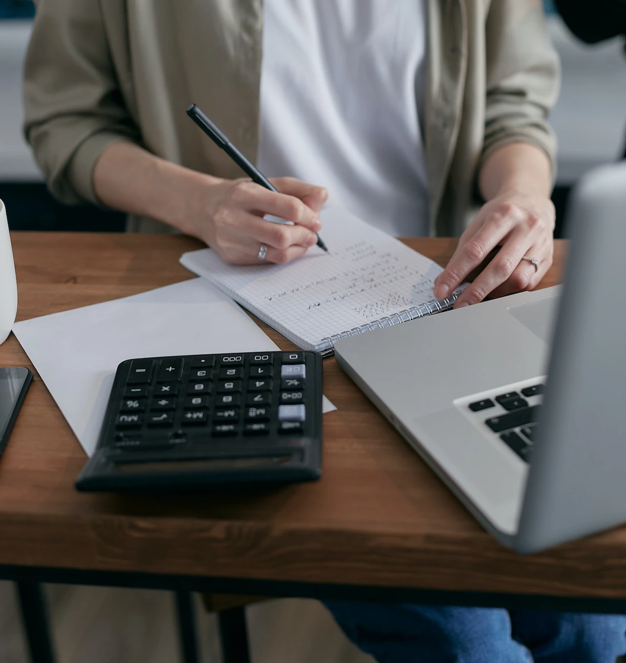 person using a calculator, notebook, and a laptop to make a budget