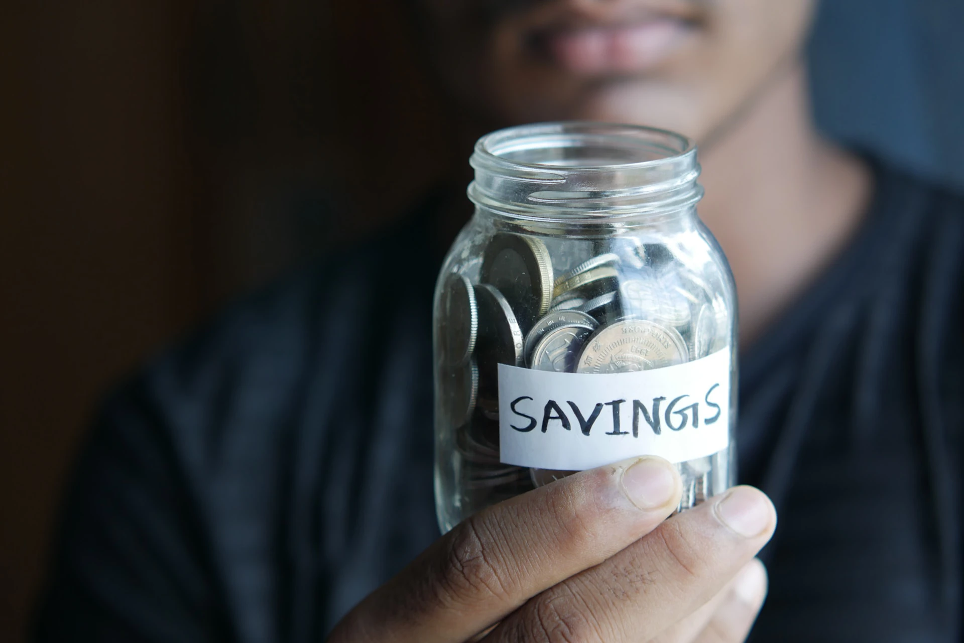 man holding up jar of coins labelled savings