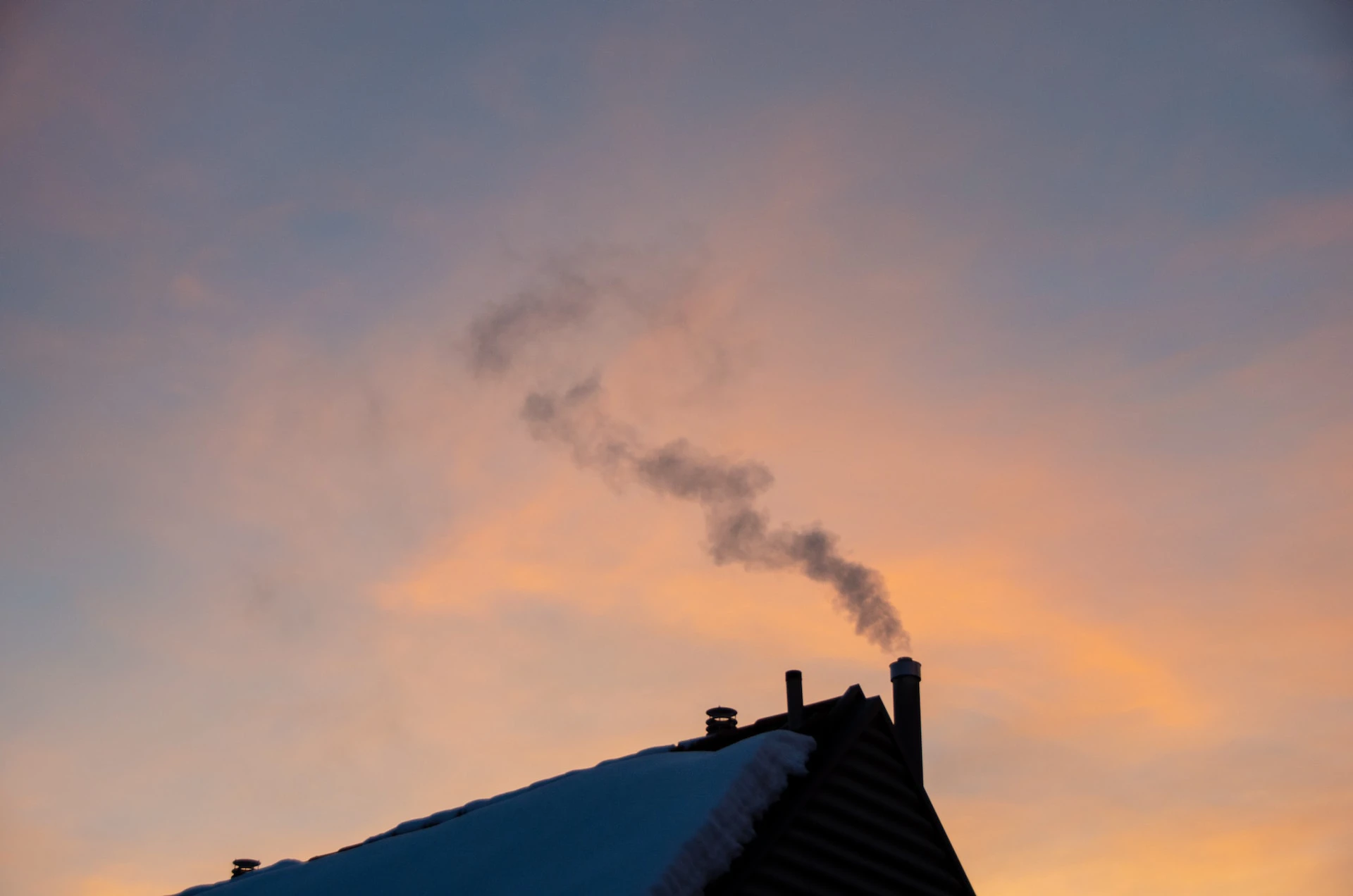 House with snow on the roof and a smoking chimney against  a sunrise