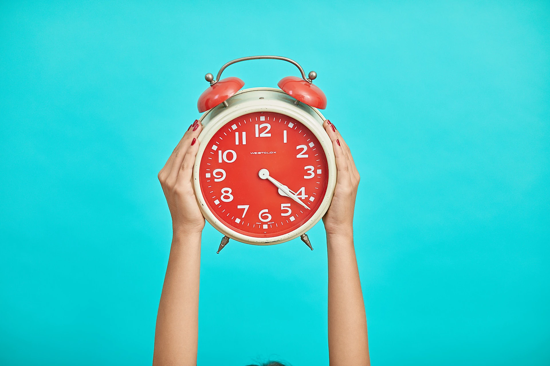 person holding red and beige alarm clock against blue background