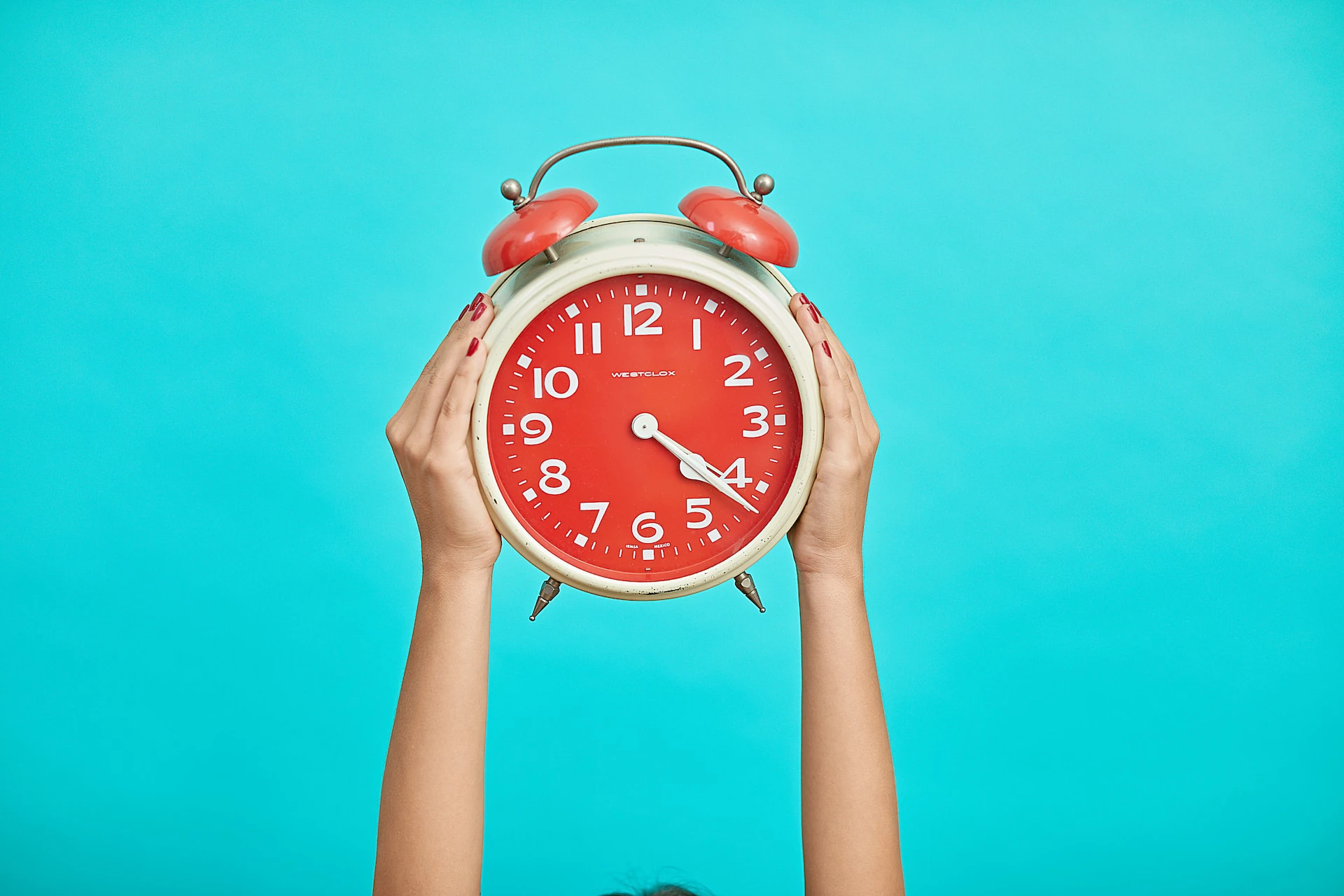 person holding red and beige alarm clock against blue background