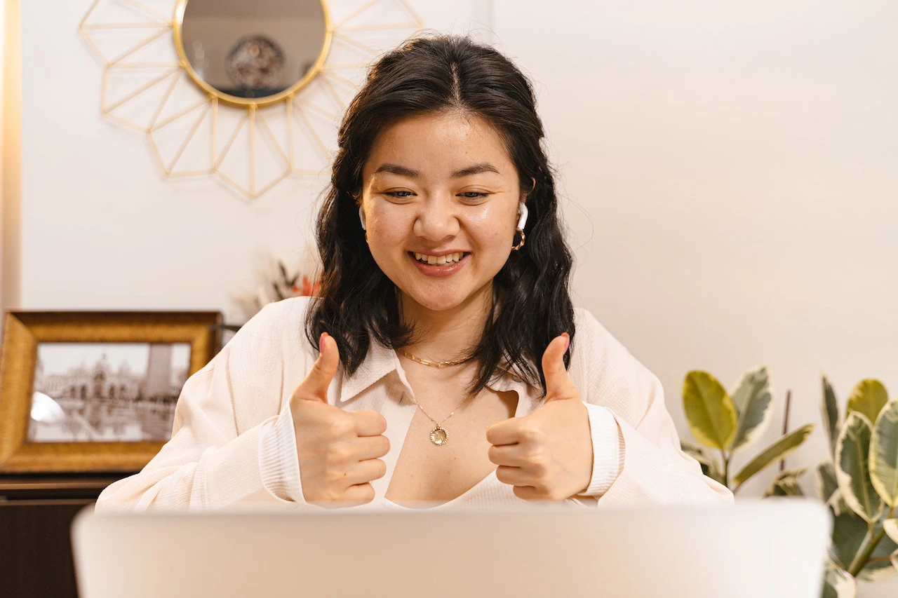 woman holding hands up in front of computer screen giving a thumbs up