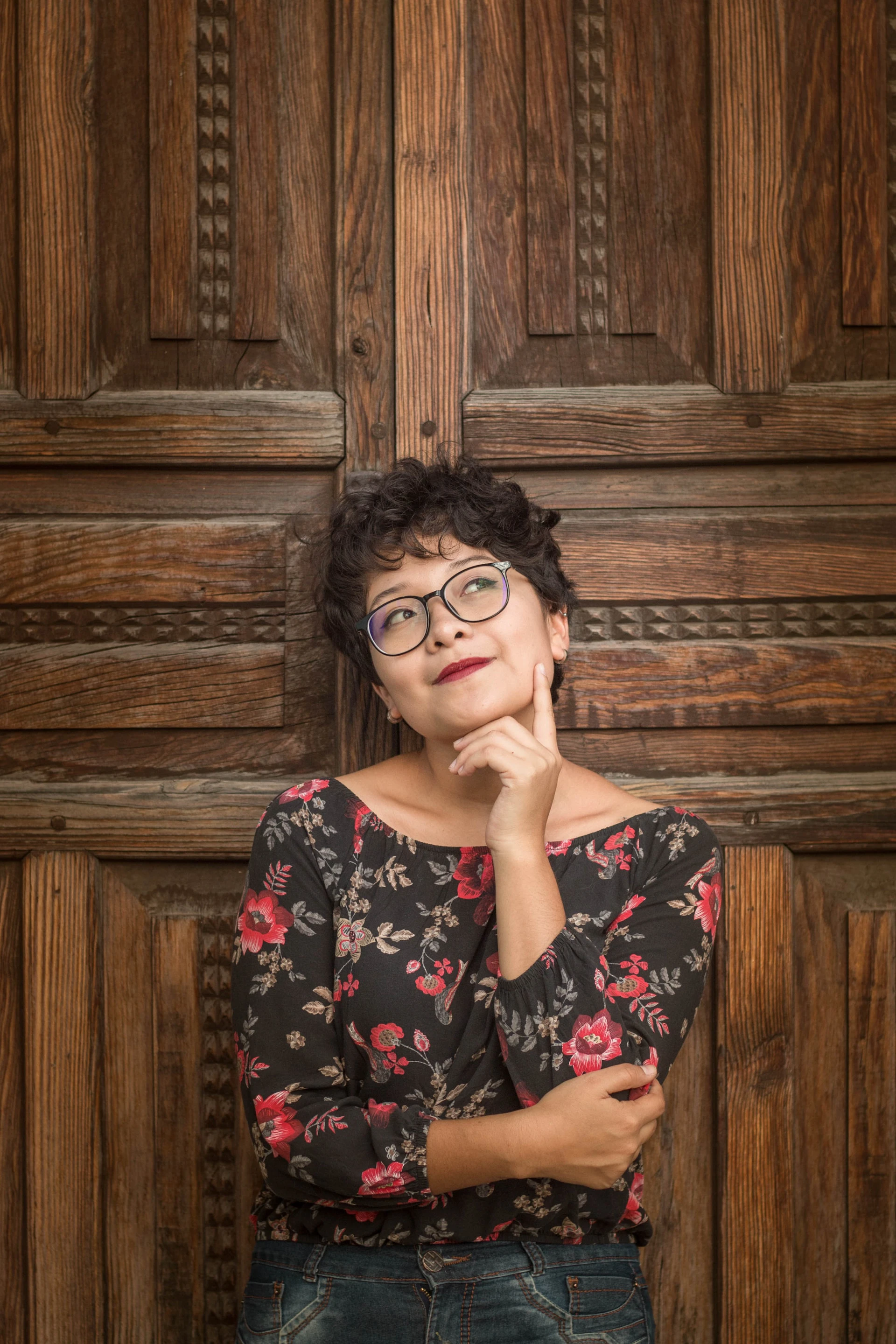 woman standing against wooden wall thinking with finger on her chin