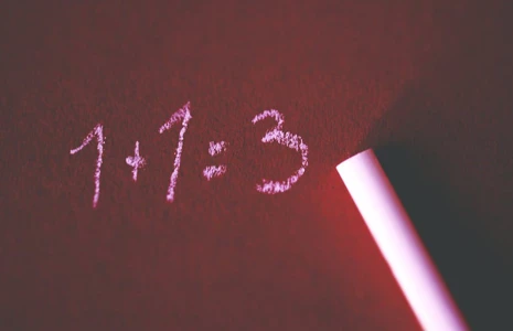 1+1 = 3 written in chalk on red tinted chalkboard