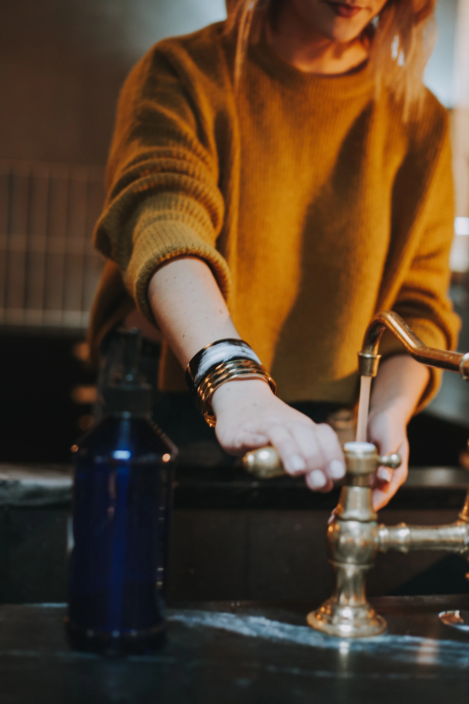 woman in mustard jumper running a vintage looking tap