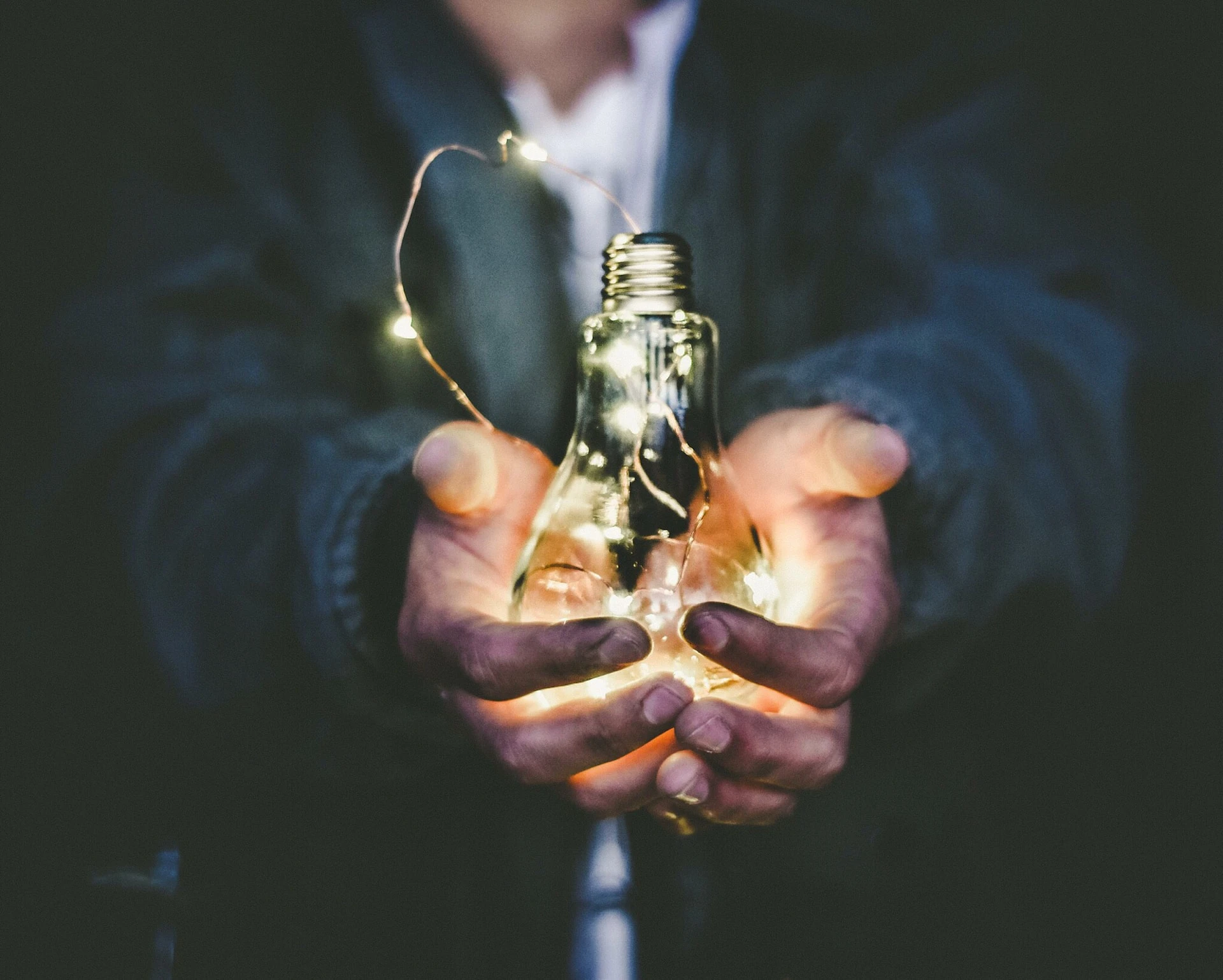 man holding light bulb with fairy lights inside