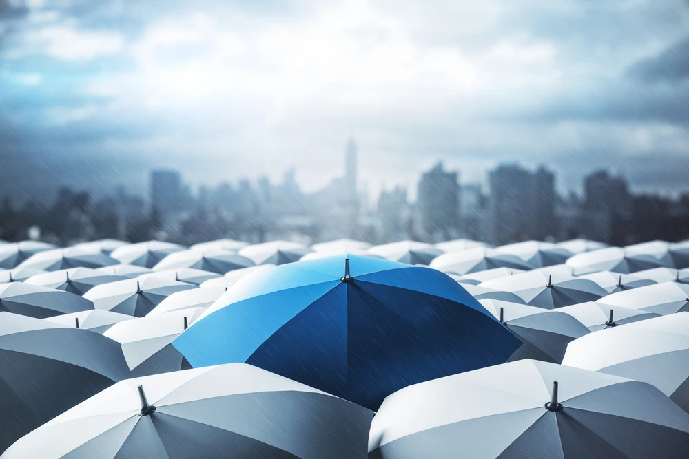 Blue umbrella on top of other gray umbrellas on city background