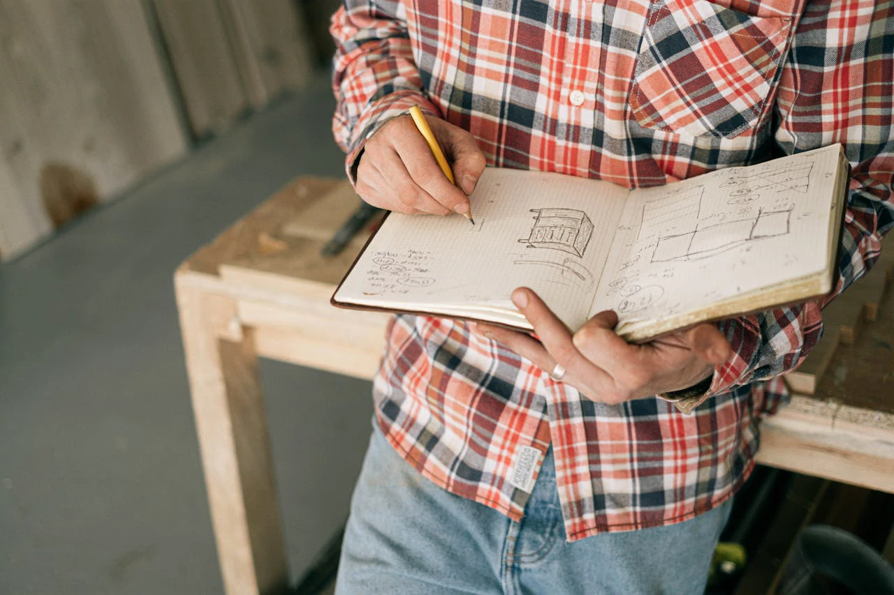 man holding a notebook sketching in design plans for furniture