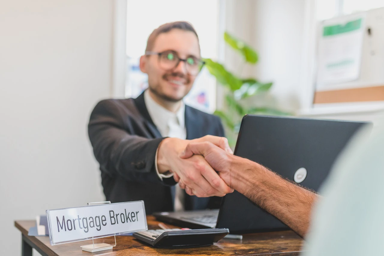 mortgage broker shaking hands with a client whilst sat at his desk