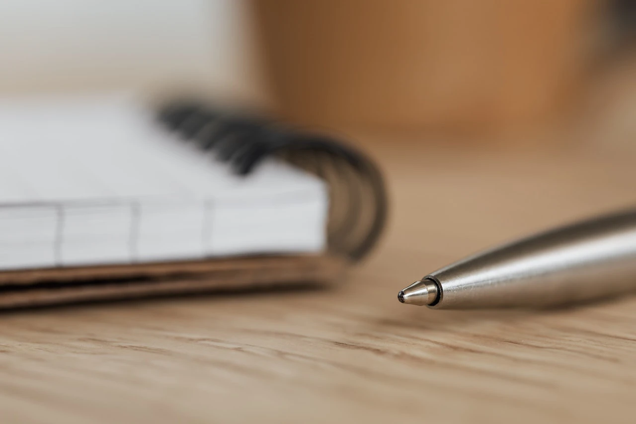 close up of the corner of a notebook and the tip of a ballpoint pen