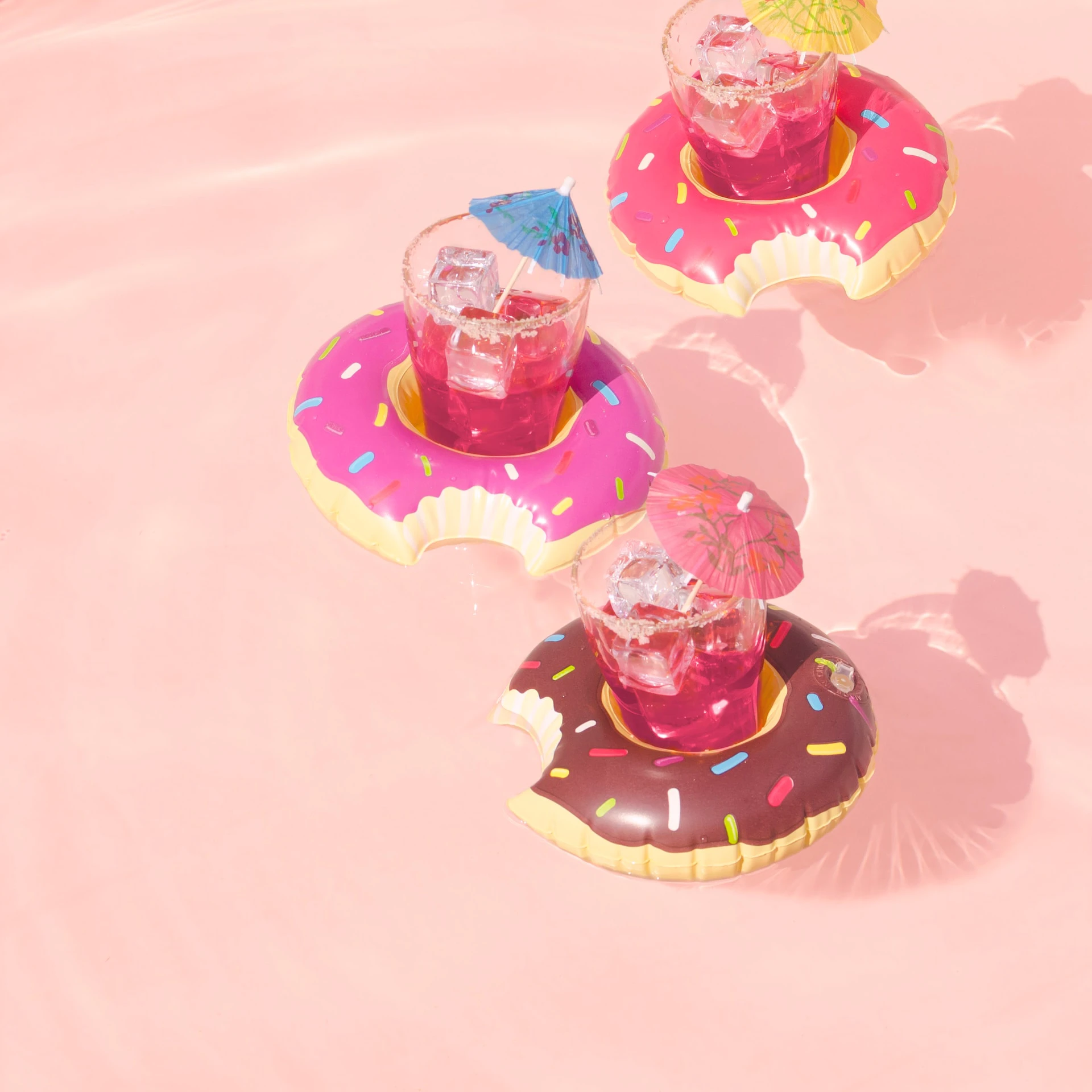 inflatable doughnuts floating on pink water with pink drinks and umbrellas in the middle