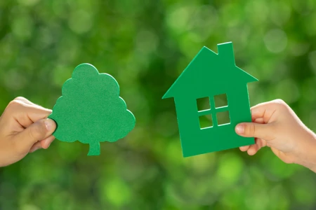 Children holding eco house in hands against spring green background