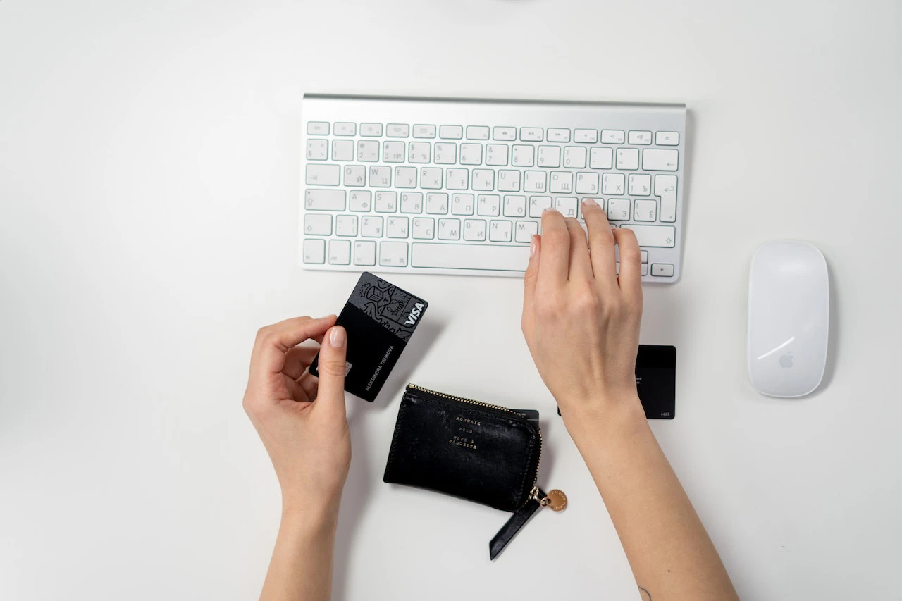 Someone typing on an Apple keyboard while holding a credit card in their other hand