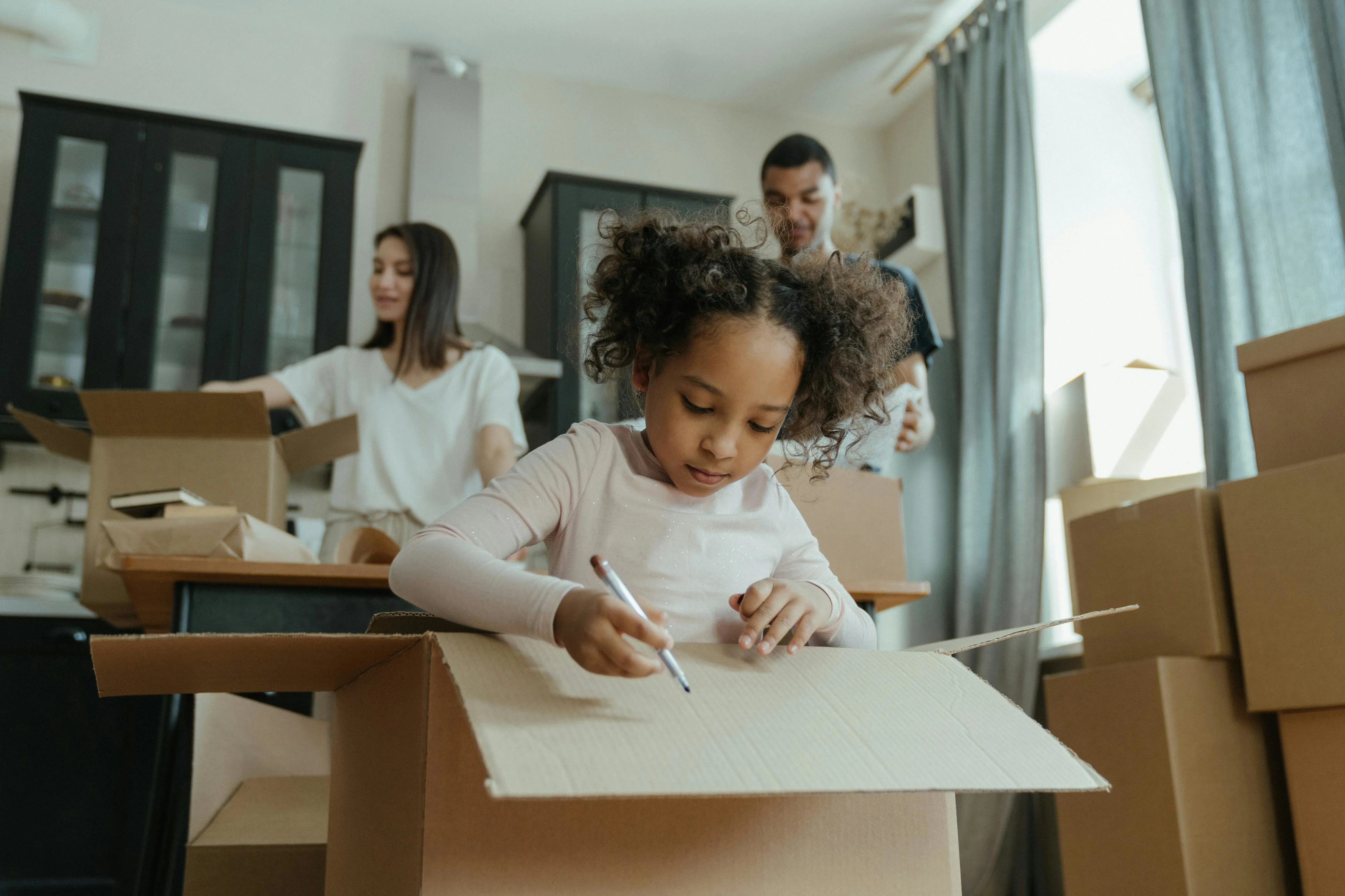 family with child moving into new home unpacking and drawing on boxes