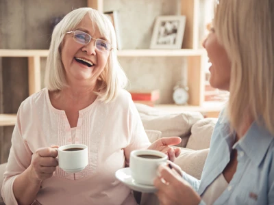 Older woman having a coffee and smiling with younger woman