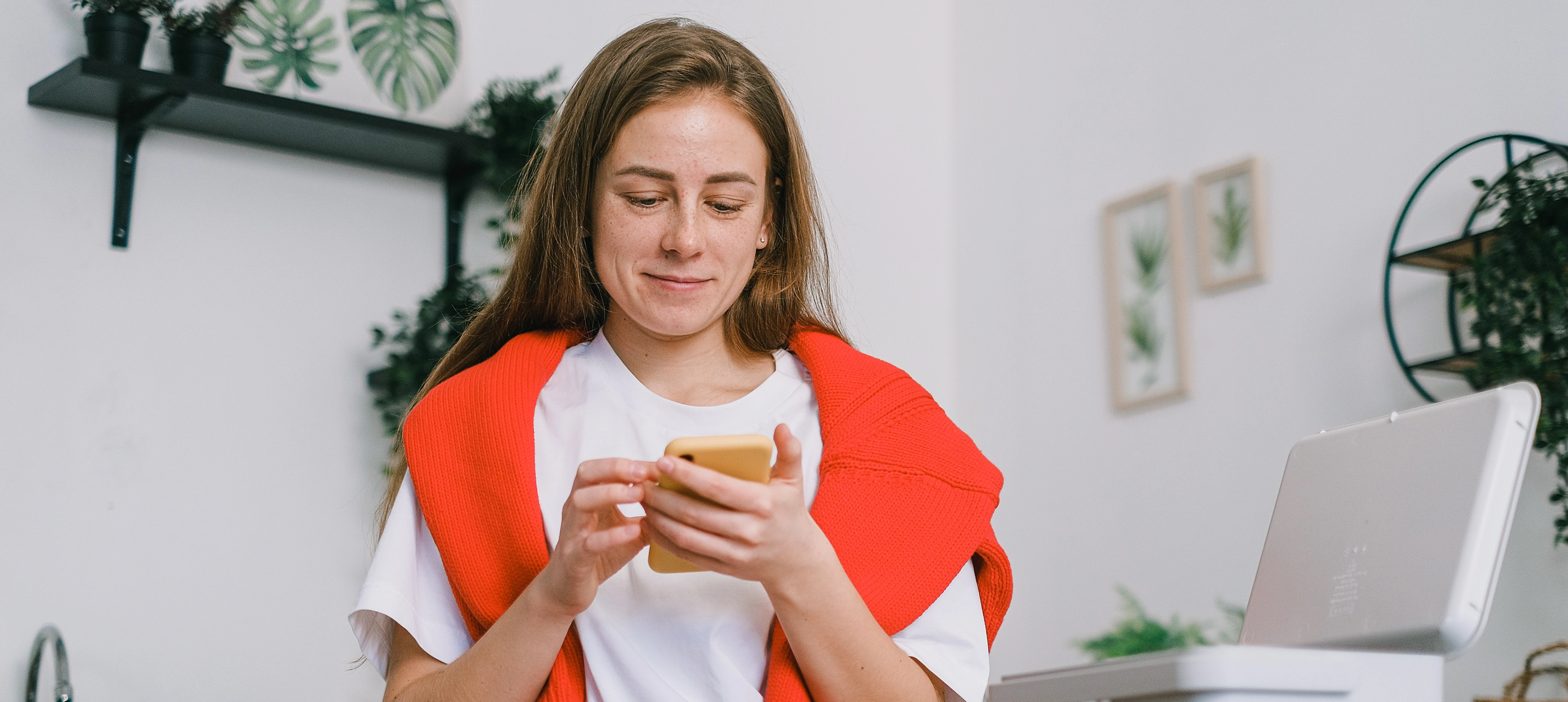 woman in white t shirt in kitchen holding a phone and looking at it