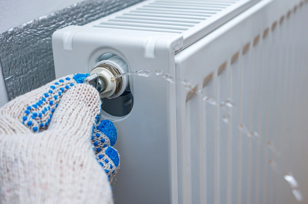 a person wearing a glvoe and bleeding a radiator