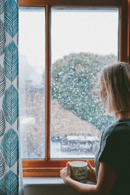 woman looking out window into snowy exterior