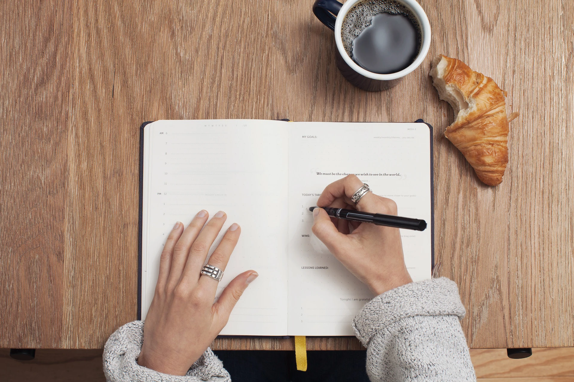 hands writing in a journal with coffee and a croissant on the table