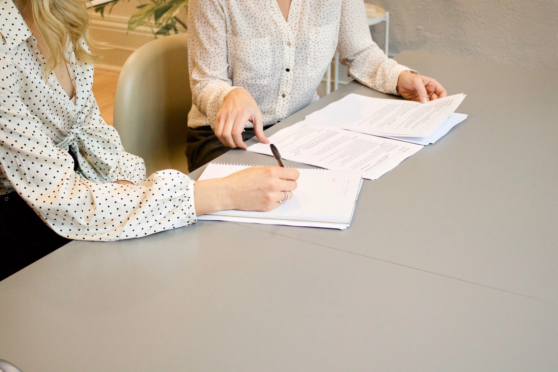 papers on grey desk being reviewed by two woman in white shirts