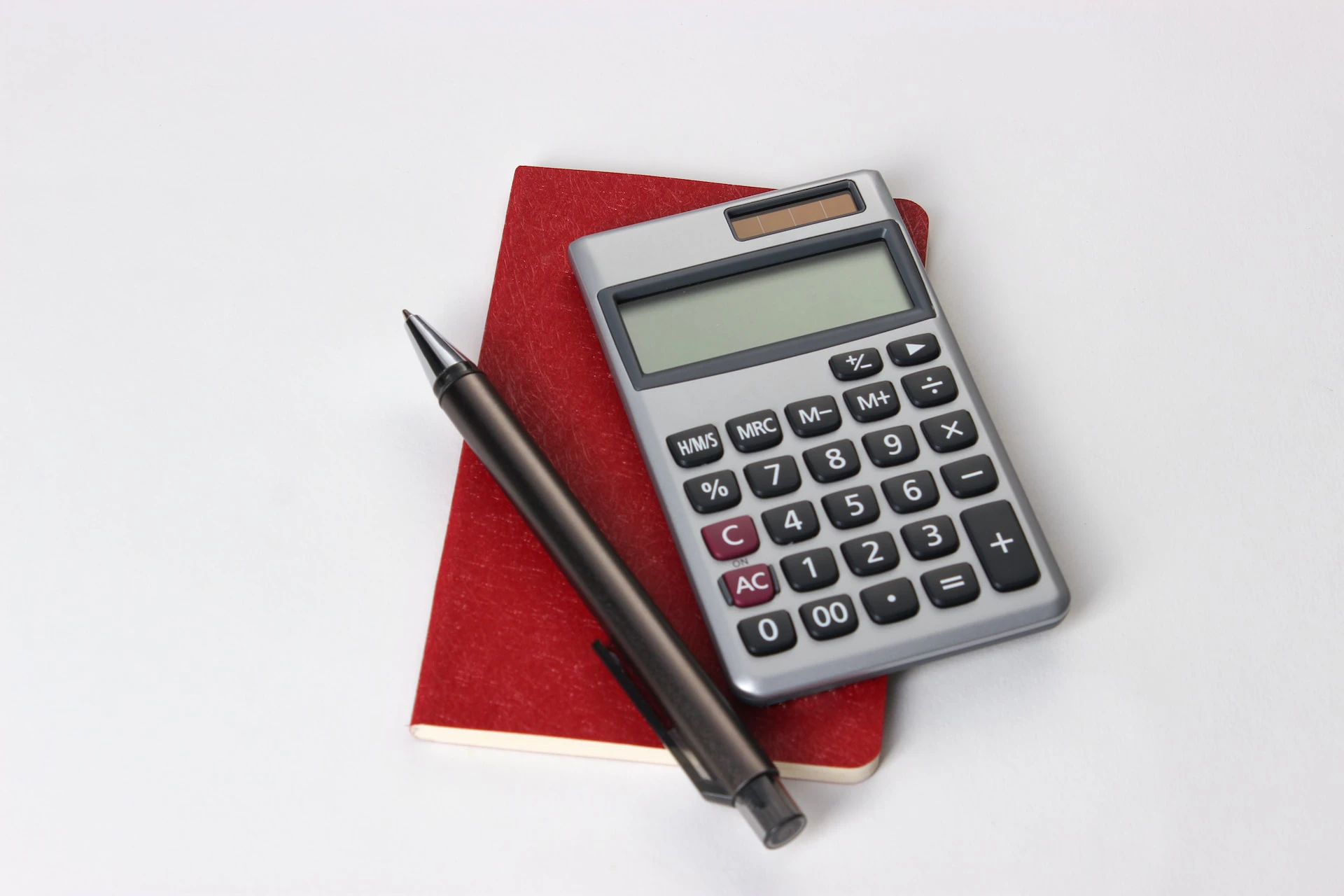 silver and black calculator sitting on red notebook next to pen