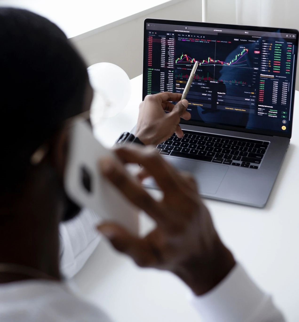 Man pointing to a graph on a laptop screen whilst using his mobile phone