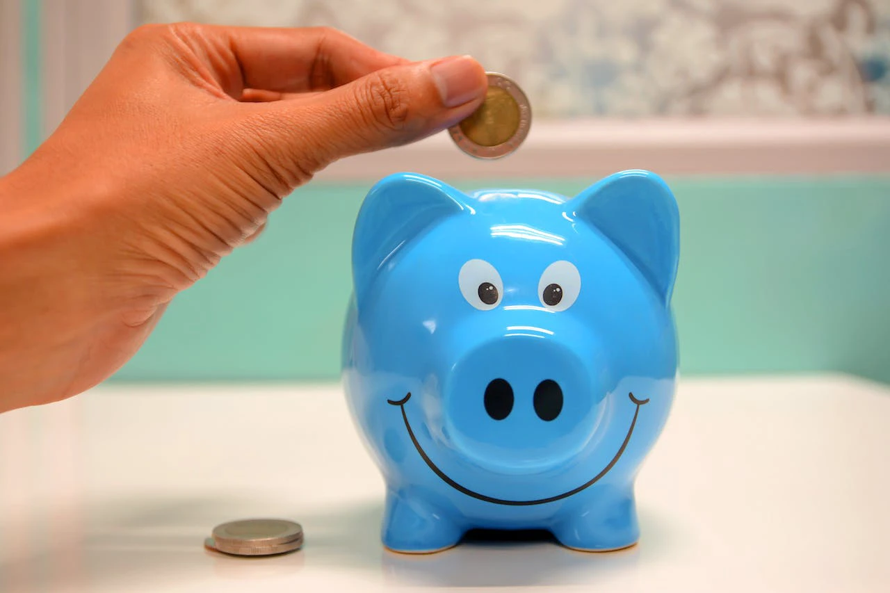 smiling blue piggy bank with someone putting money in the top