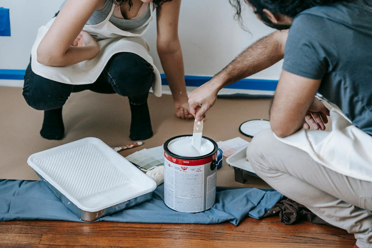 a couple crouching next to a tin of white paint, ready to paint a wall