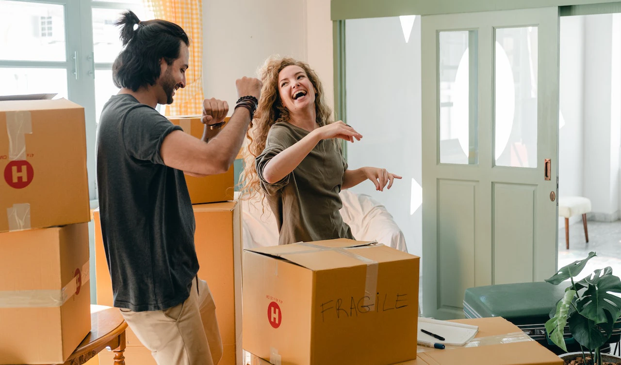 two people laughing and dancing around moving boxes
