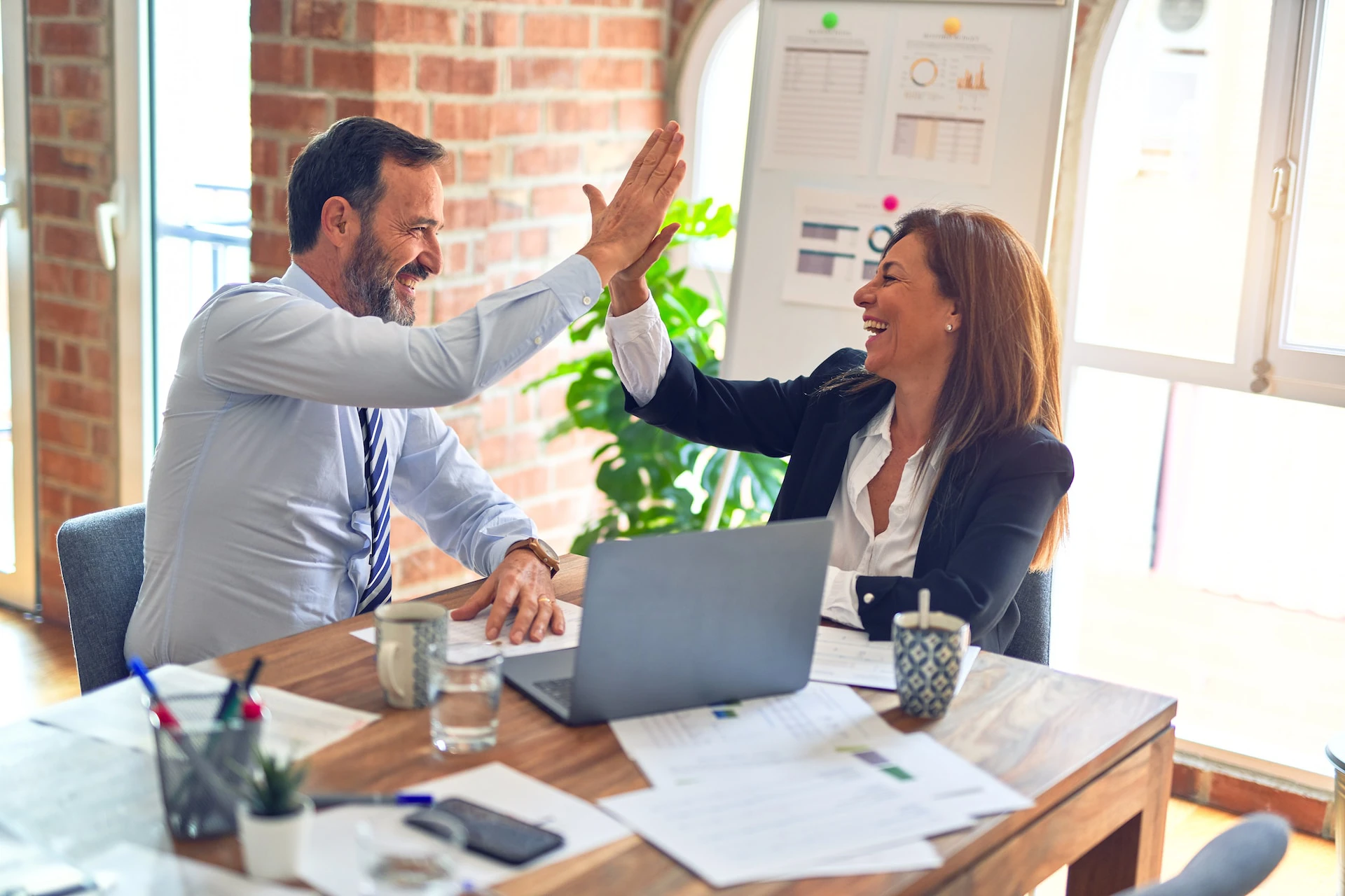 two people in business attire high fiving over a laptop