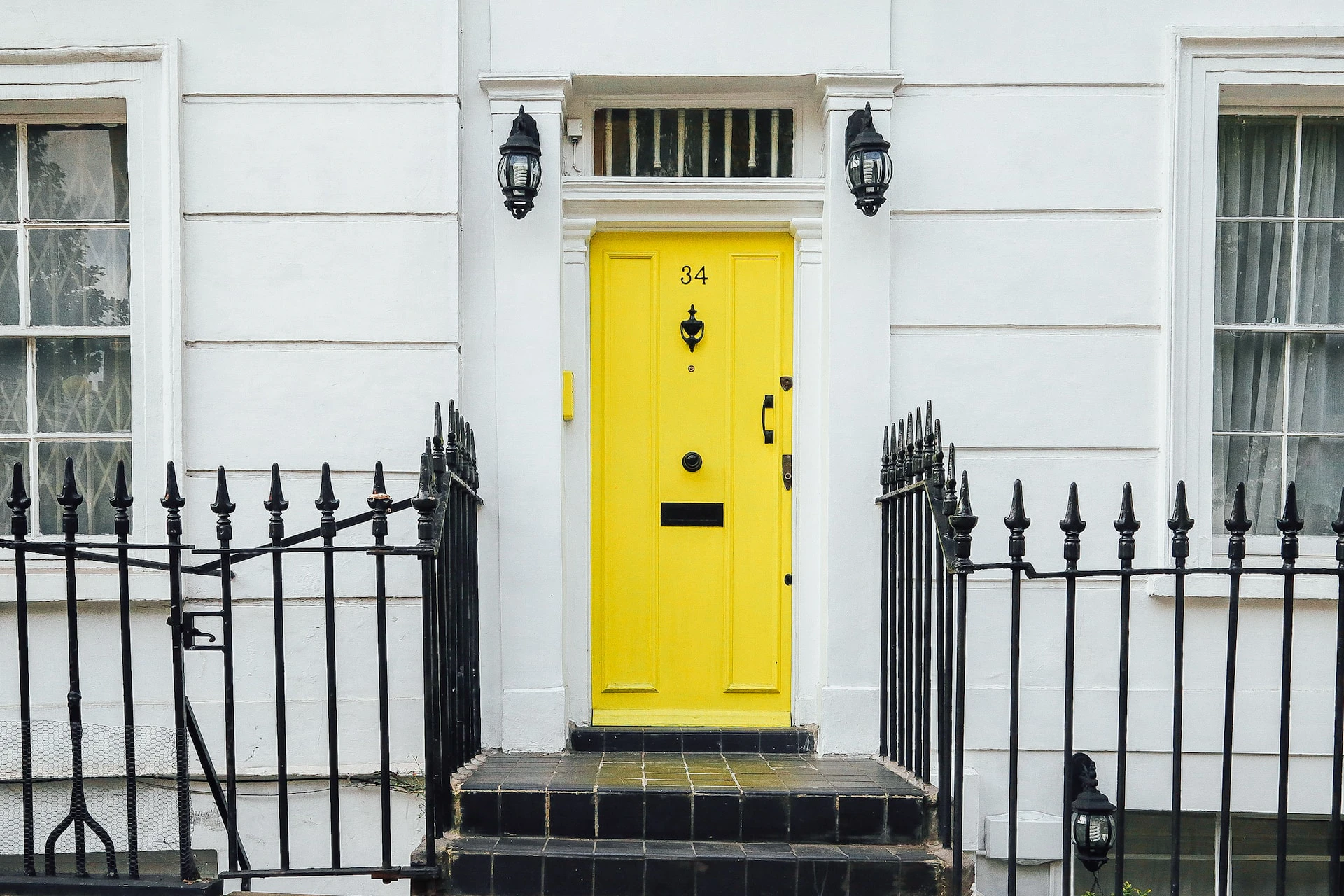 yellow door against a white wall with black fence