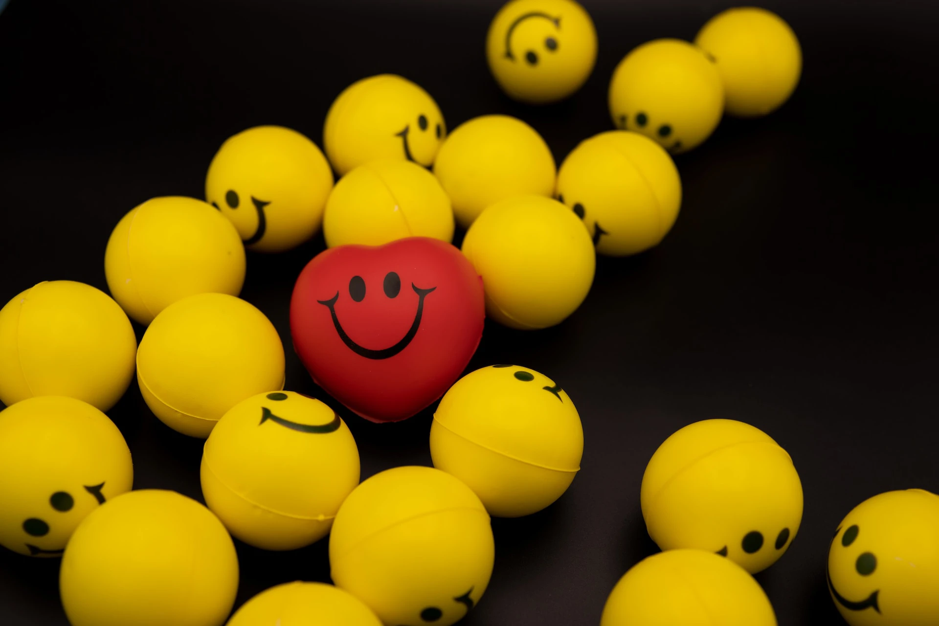 Red heart smiley face ball sitting around yellow smiley face balls