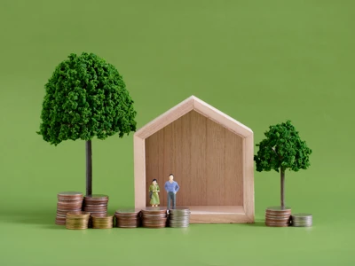 Model house with miniature people and coins on green background