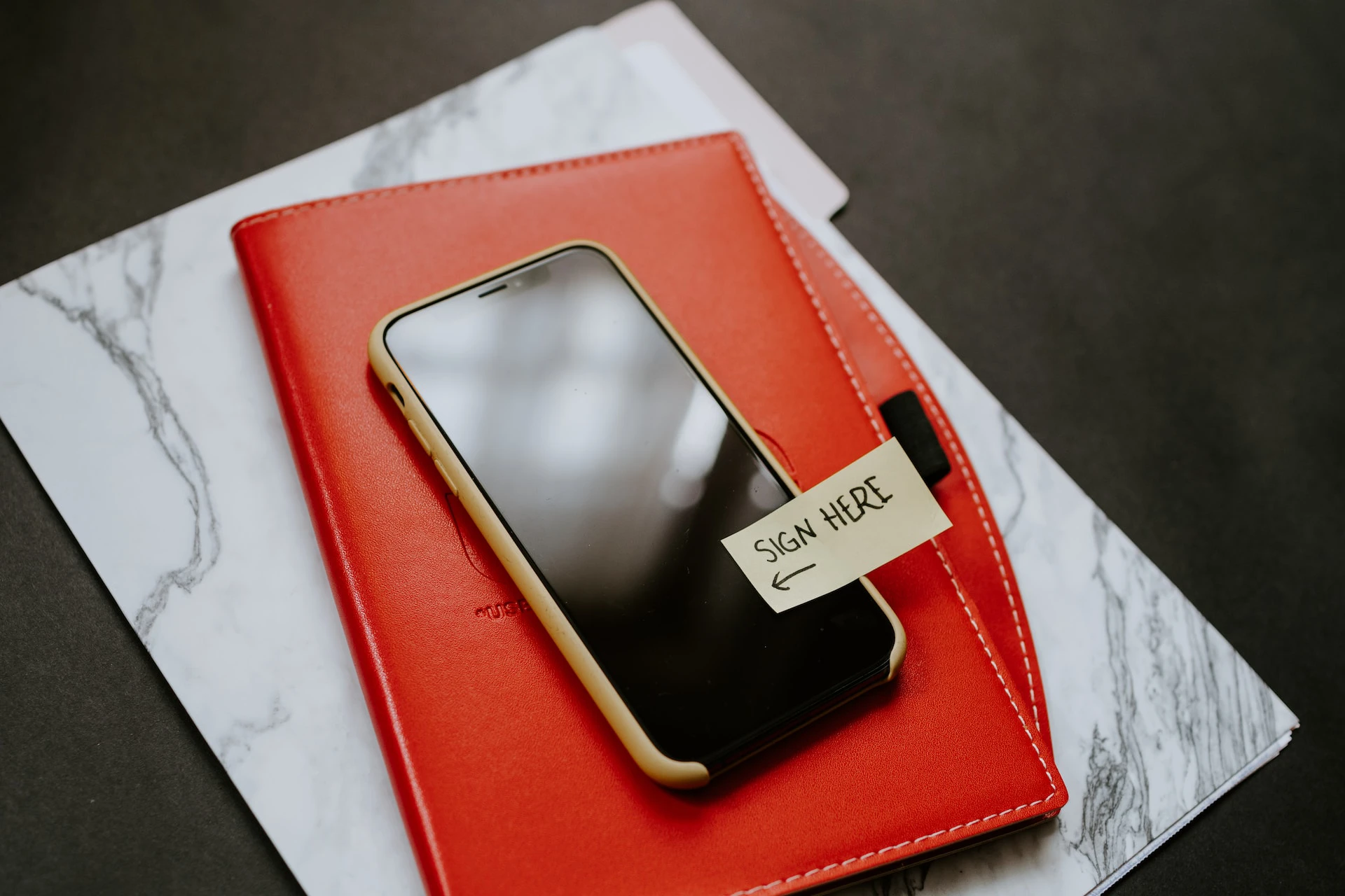 phone with sign here sticky label on it lying on top of red folder