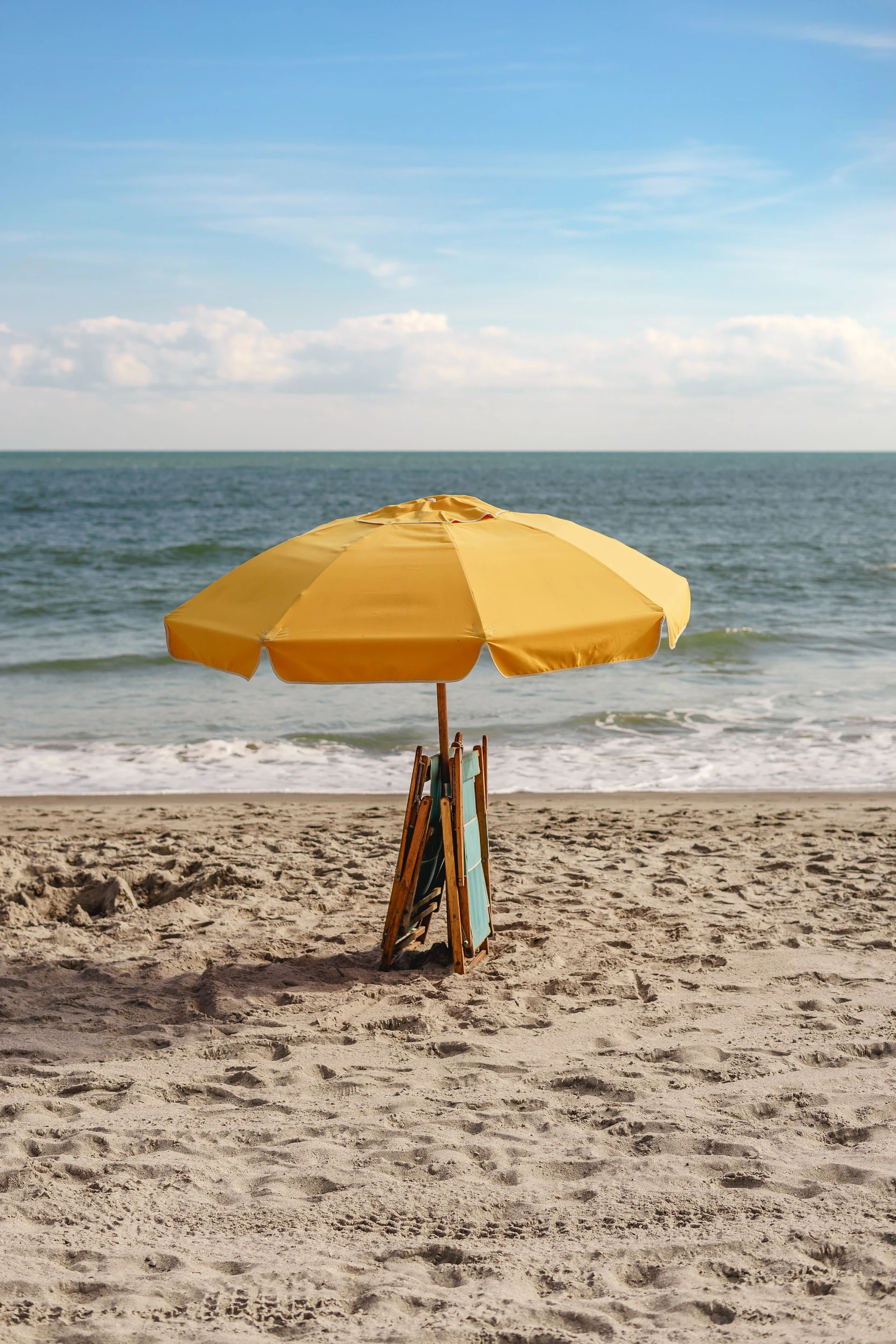 yellow umbrella and folded deck chair on beach with ocean in background