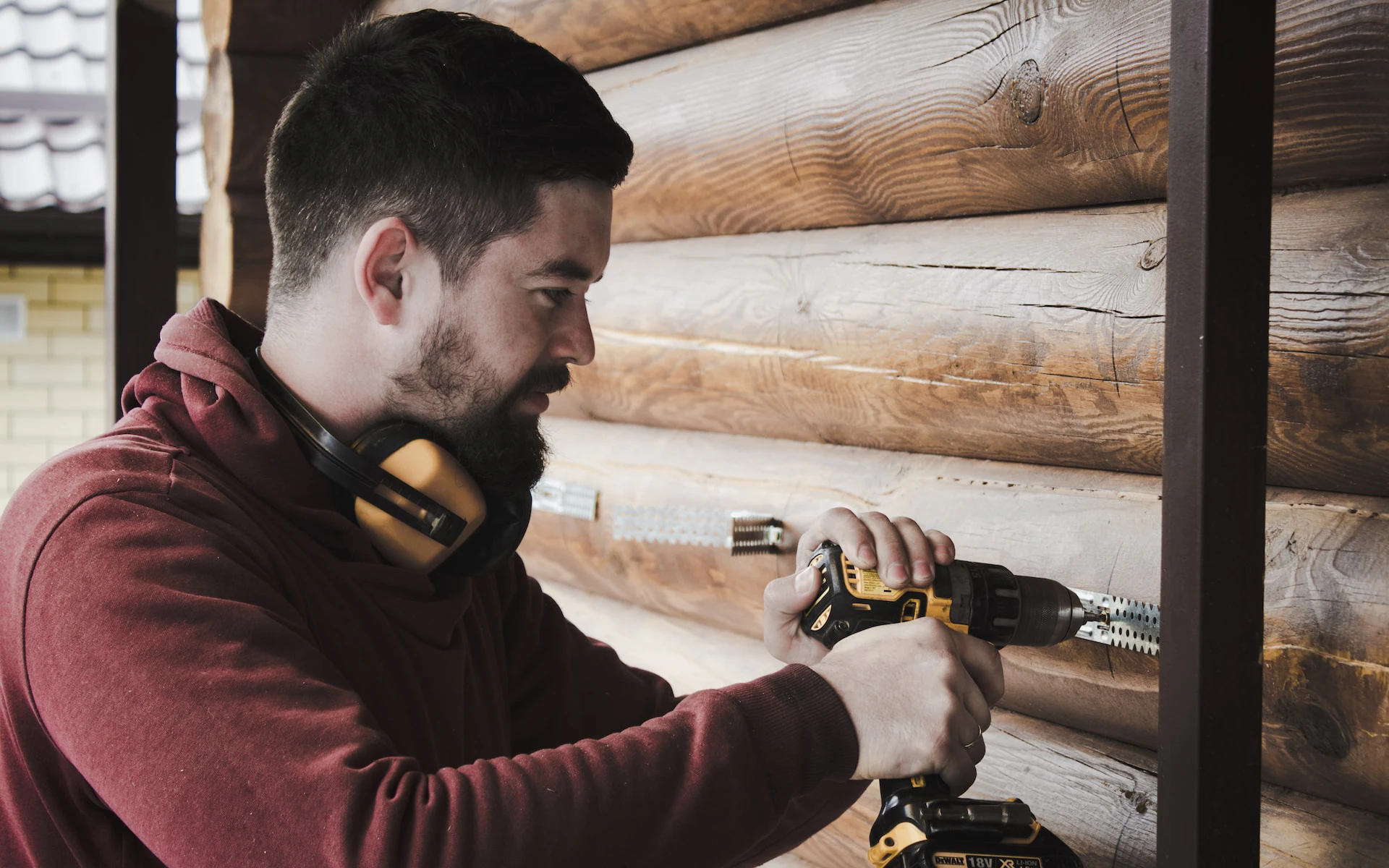 man in maroon hoodie drilling into wooden wall