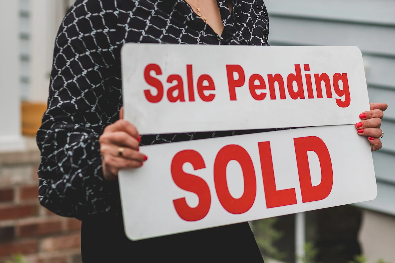 Person holding two signs, one reads 'sale pending' and the other reads 'SOLD'