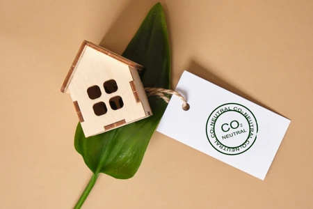 green leaves, miniature wooden house model and white tag with co2 neutral marking on brown background