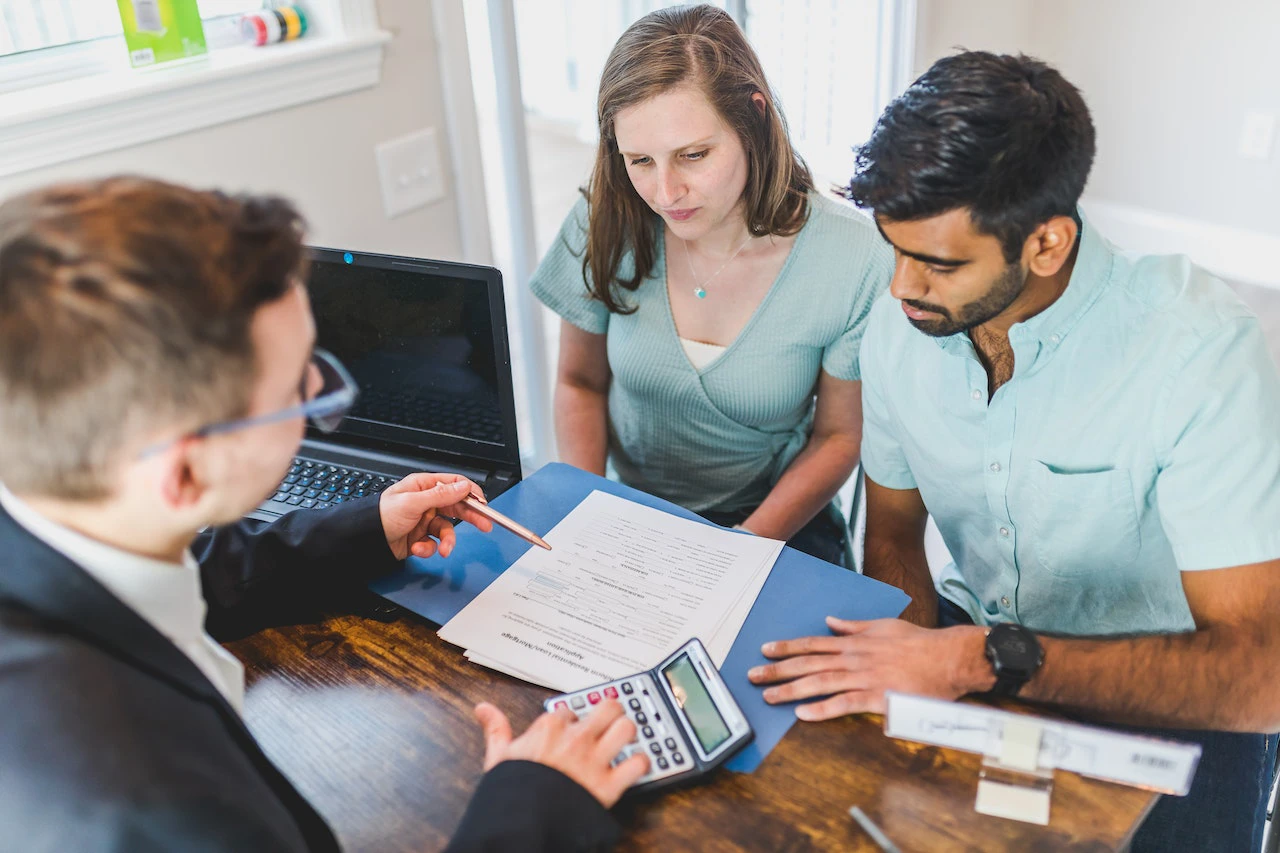 Man meeting with a couple over a calculator, laptop, and paper forms