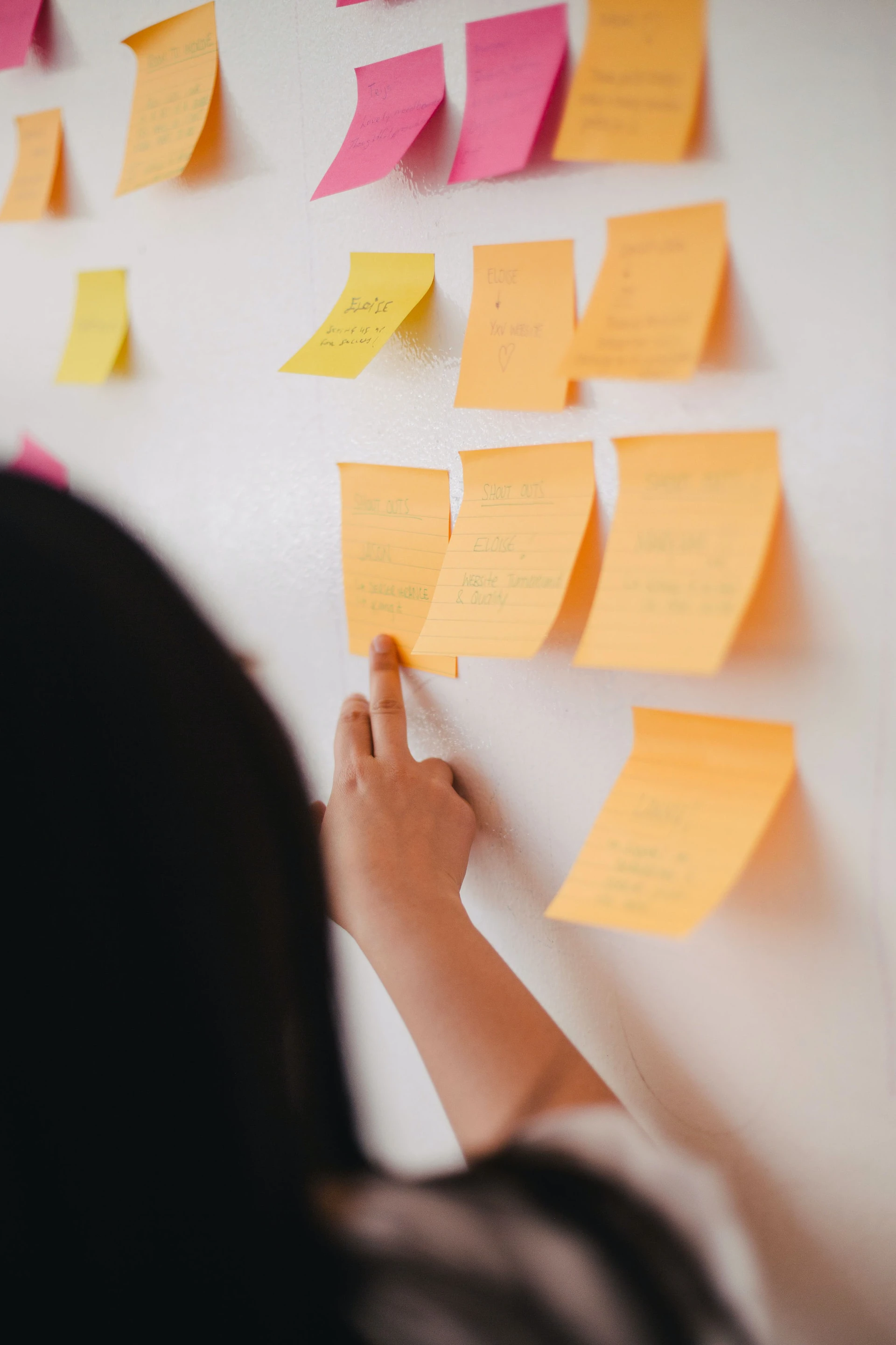 woman pointing at orange sticky notes on a wall