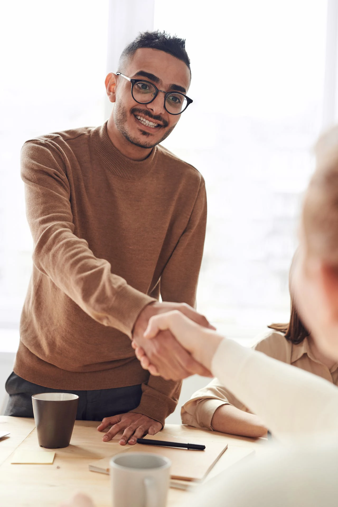 photo of a man wearing a brown jumper and glasses shaking a woman's hand