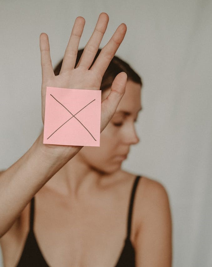 Woman holding up hand with pink post it note and a cross stuck on palm