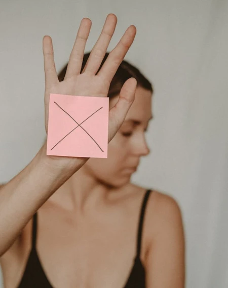 Woman holding up hand with pink post it note and a cross stuck on palm