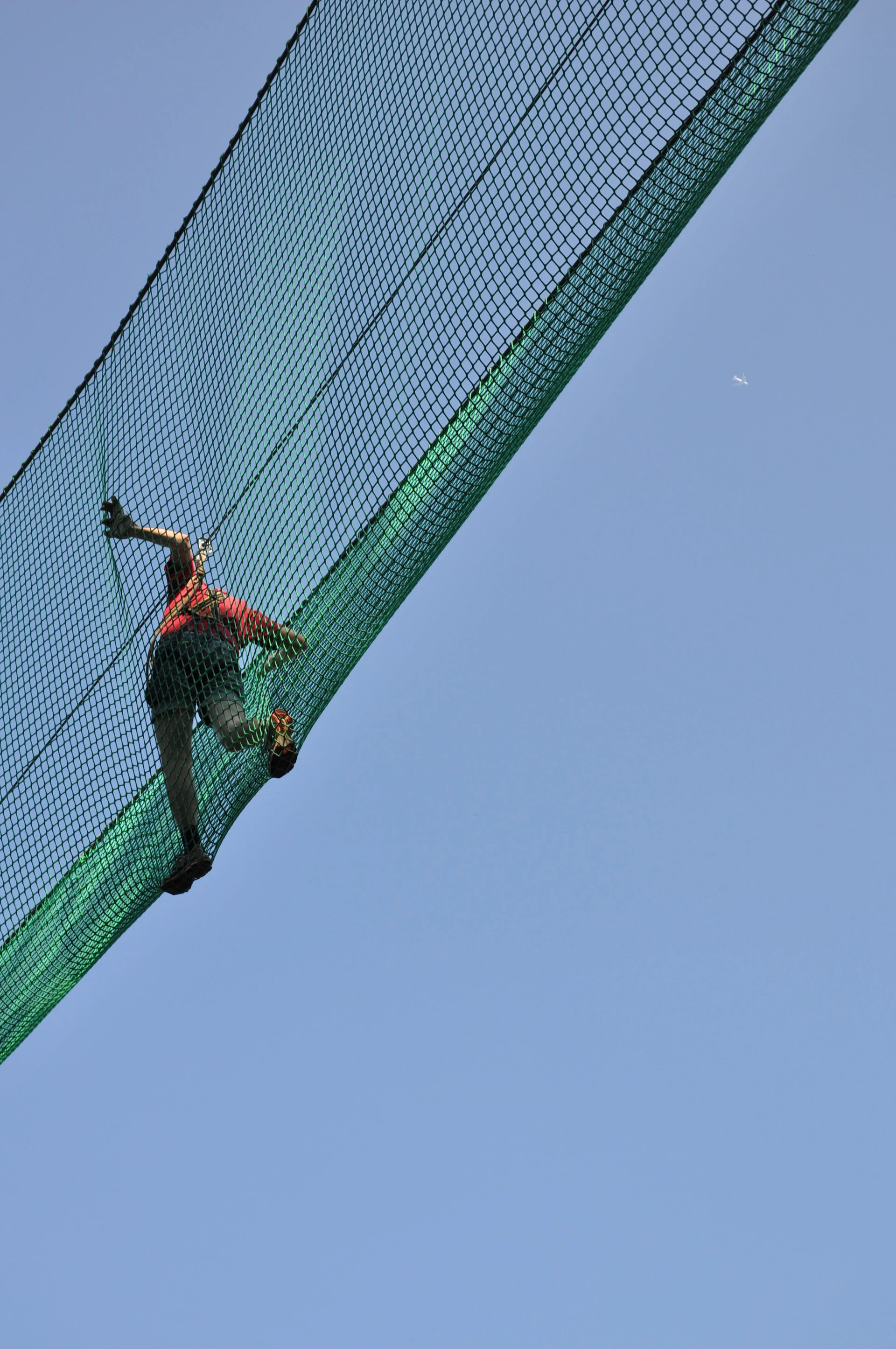 woman in red shirt walking across green safety net under open blue sky