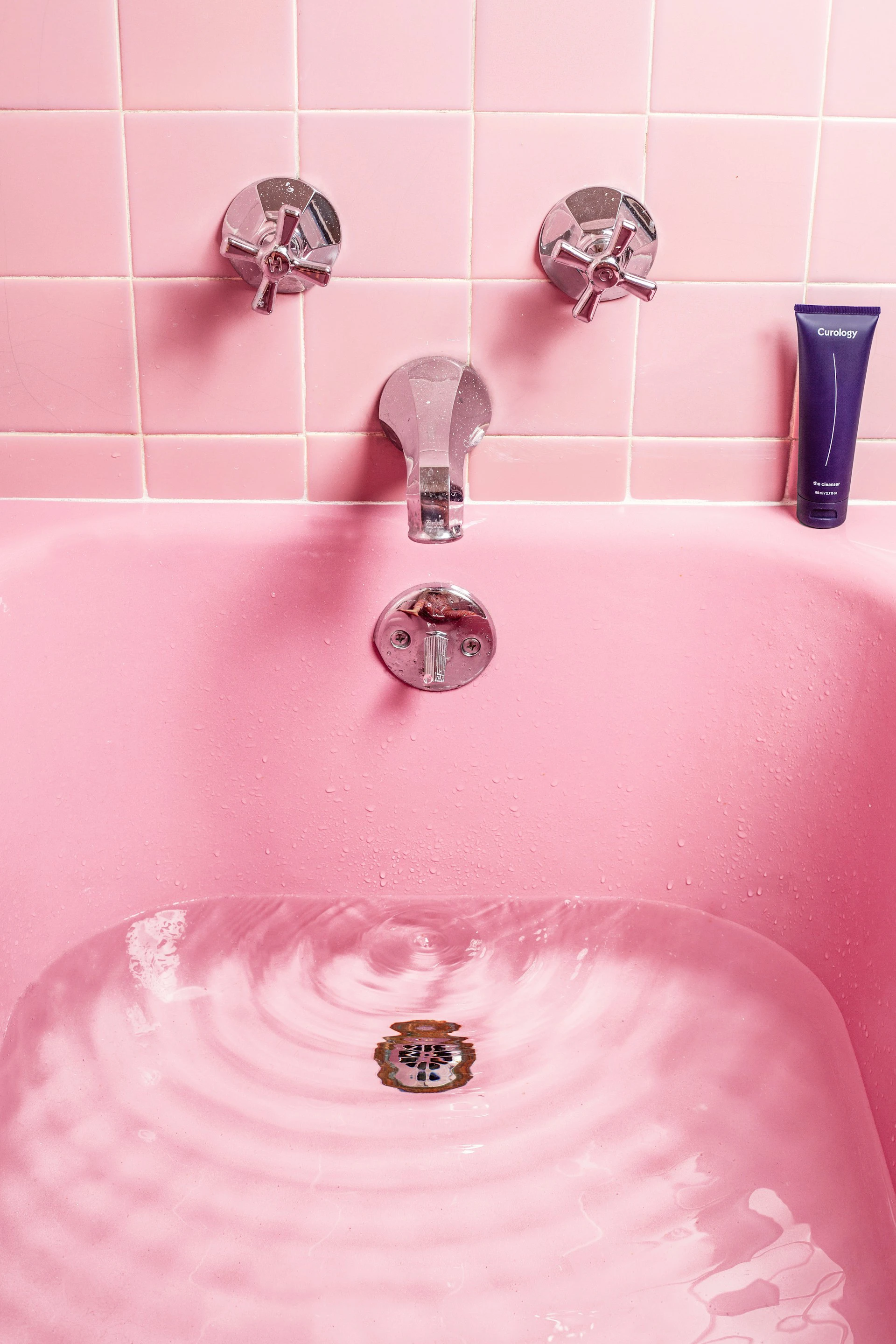 pink bathtub with water in it and pink bath tiles