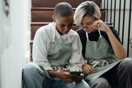 Two women looking at a smart phone while sitting on stairs
