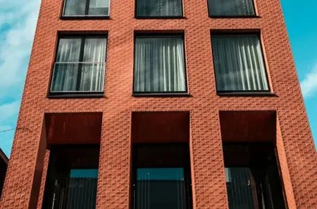 Low to high image of a block of brick flats against a blue, cloudy sky